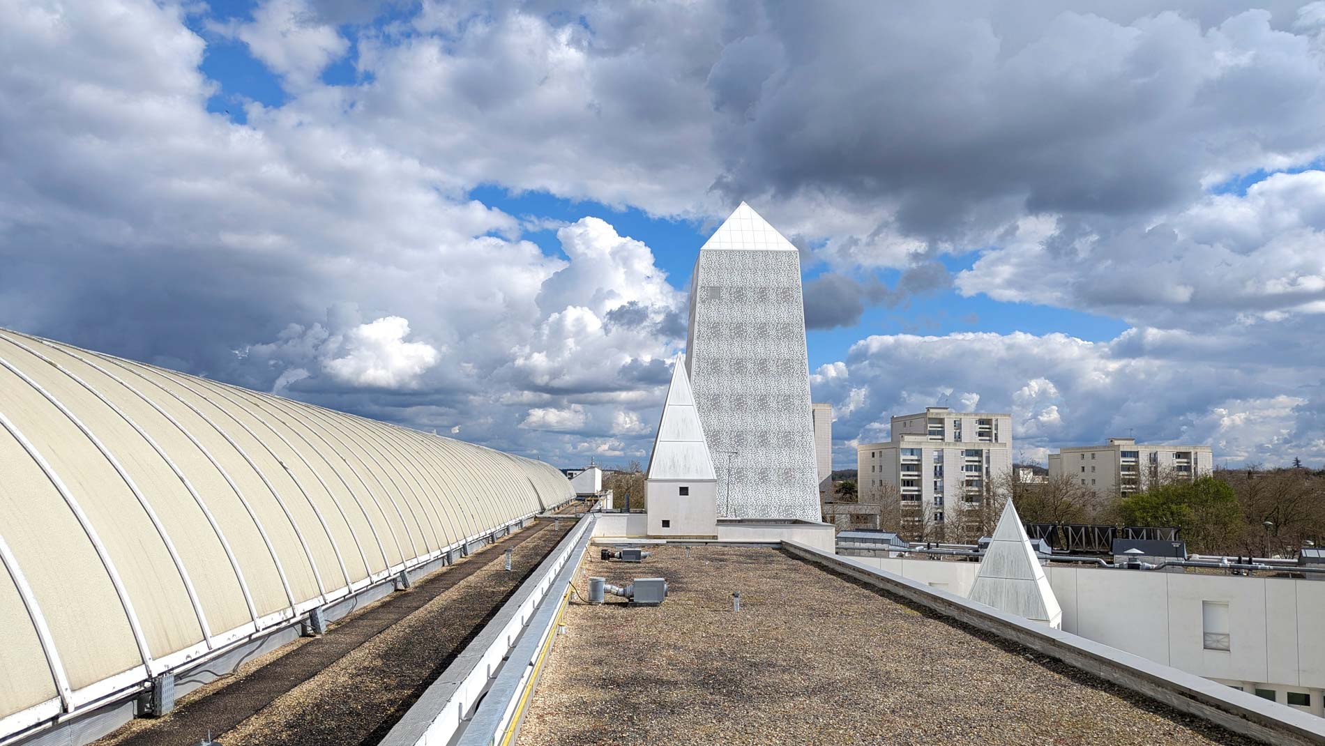 Vue depuis le toit après la rénovation : la verrière de la rue intérieure, l’obélisque et ses petites pyramides, sous un ciel nuageux